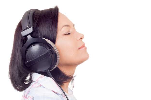 Glückliche lächelnde schöne junge Frau, die Musik mit Kopfhörern auf einem weißen Hintergrund hört