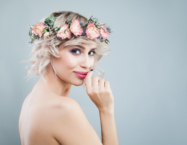 Glückliche lächelnde vorbildliche Frau, die Blumen trägt, krönen gelocktes Haar-Make-up und Blumen