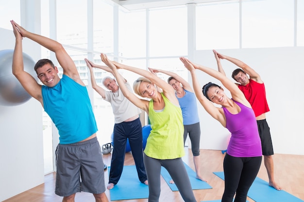 Glückliche Leute, die das Ausdehnen tun, trainieren in der Yogaklasse