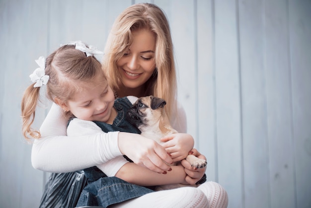 Glückliche liebevolle Familie. Bemuttern Sie und ihr Tochterkindermädchen, das entzückenden Pug spielt und umarmt