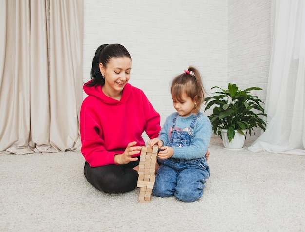 Glückliche liebevolle Familie, die mit Holzblöcken spielt und Spaß hat. Mutter und ihre Tochter spielen zusammen.