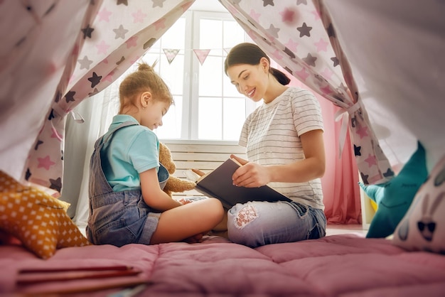 Glückliche liebevolle Familie Hübsche junge Mutter, die ihrer Tochter drinnen ein Buch vorliest