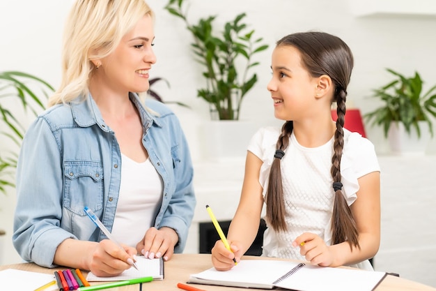 Glückliche liebevolle Familie. Mutter und ihr Tochterkindermädchen spielen und Hausaufgaben machen.