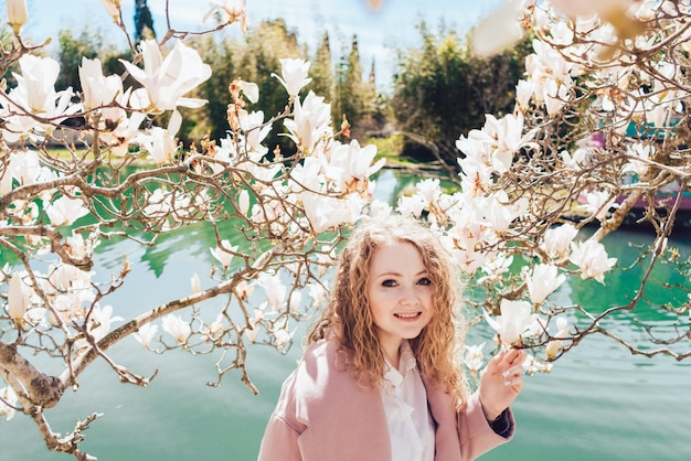 Glückliche lockige Frau, die Körper und Frühling im Park neben Teich und Magnolie genießt