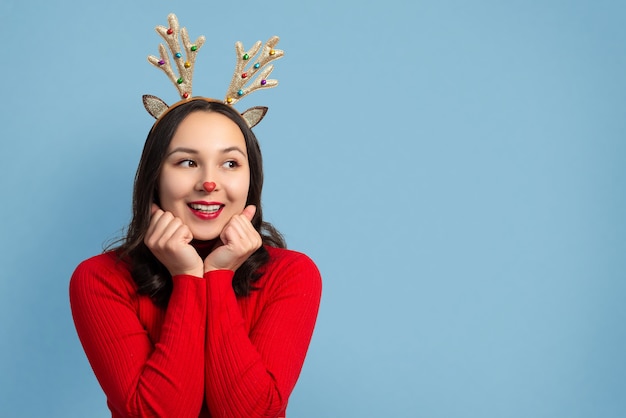 Glückliche lustige Frau mit Weihnachtshirschhörnern auf einem blauen Hintergrund.