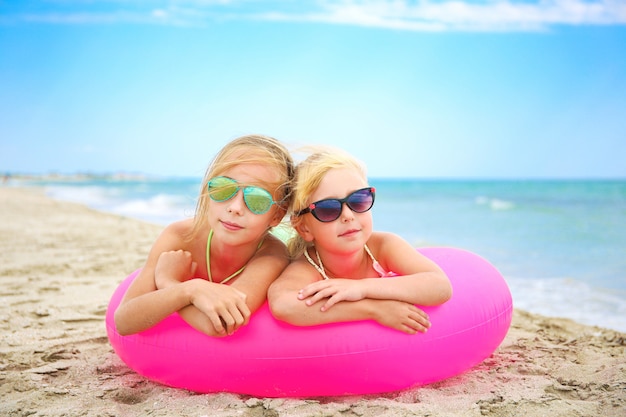 Glückliche Mädchen, die auf rosa aufblasbarem Kreis am Strand liegen