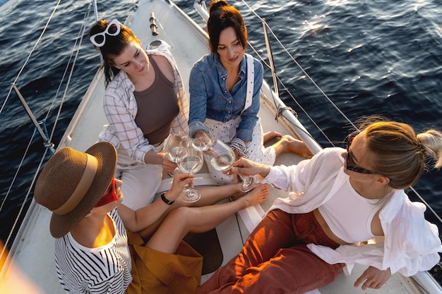 Glückliche Mädchen Freunde trinken Weißwein auf dem Segelboot während des Segelns im Meer