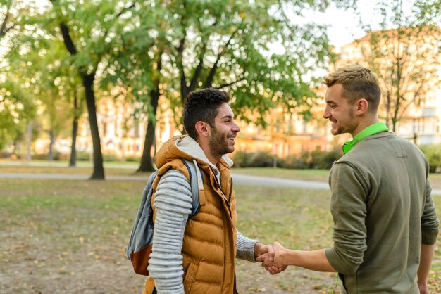 Foto glückliche männliche freunde schütteln sich die hände, während sie im park stehen