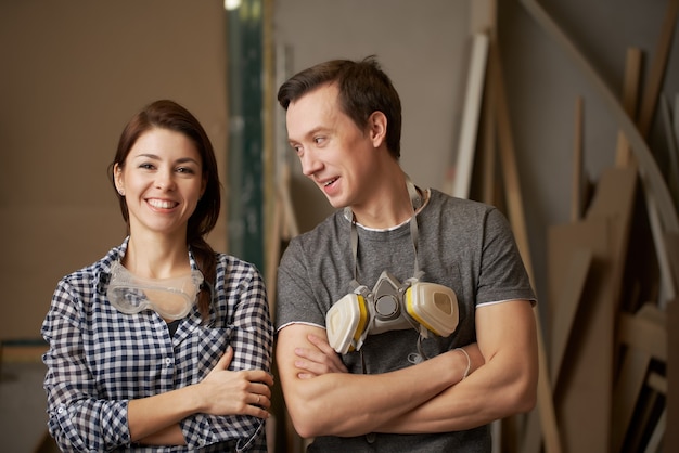 Glückliche männliche und weibliche Schreiner mit verschränkten Armen in der Werkstatt