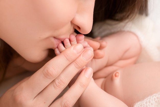 Glückliche Mama küsst liebevoll die Zehen eines Neugeborenen. Foto in hoher Qualität