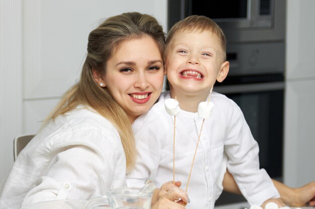 Glückliche Mama und Sohn setzen Marshmallows am Stiel auf