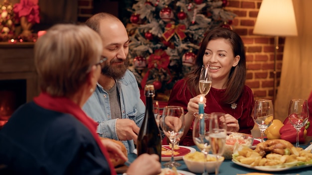 Glückliche Menschen, die miteinander reden, während sie das Weihnachtsessen zu Hause genießen. Festliche, fröhliche Familienmitglieder, die den Winterurlaub feiern, während sie traditionelle hausgemachte Speisen essen und plaudern.