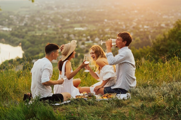 Glückliche Menschen haben Spaß, lächeln und trinken Weißwein. Junge Freunde sitzen am Sommertag auf dem Gipfel des Berges.