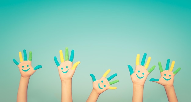 Glückliche Menschen mit Smiley auf den Händen vor blauem Sommerhimmel