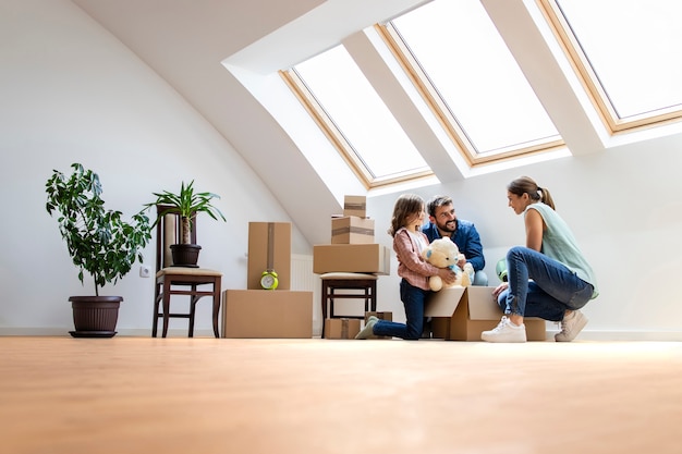 Glückliche moderne Familie, die in ein neues Haus einzieht und zusammen Kisten auspackt.