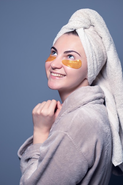 Glückliche moderne Frau mit Augenflecken. Mädchen in einem Handtuch auf dem Kopf, Schönheit, Hautpflege.