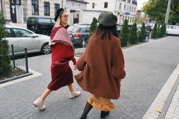 Glückliche Momente mit zwei stilvollen Mädchen, die auf Straße in der Stadt gehen. Nahaufnahmeporträt, lustige freudige attraktive junge Frauen, die Spaß haben, lächelnd, schöne Momente, beste Freunde, Schwestern.