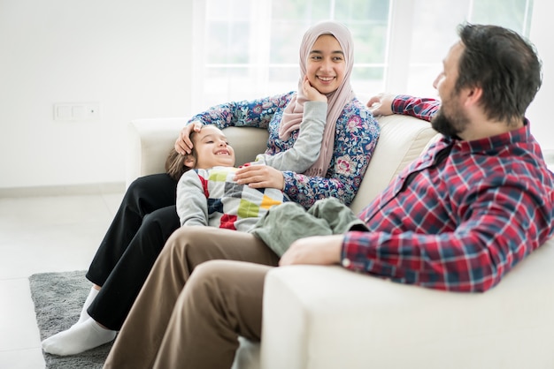 Glückliche moslemische Familie, die zu Hause auf Sofa in lebendem Roome sitzt