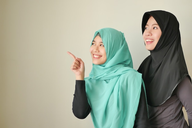 Glückliche moslemische Frau, lächelnde islamische Frauen, die oben zeigen; muslimische Mädchen zeigen nach oben; schöne asiatische muslimische frauen mit hijab oder kopftuch, die mit dem finger zeigen oder die hand auf den leeren raum zeigen