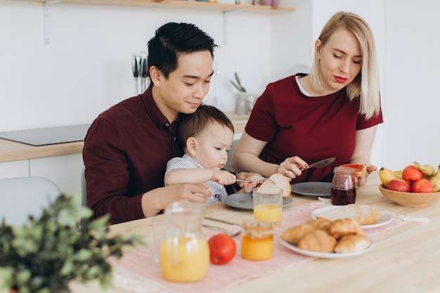 Glückliche multikulturelle Familie. Asiatischer Vater und seine kaukasische blonde Frau frühstücken mit ihrem schönen Sohn in der Küche.