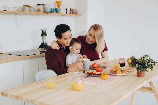 Glückliche multikulturelle Familie. Asiatischer Vater und seine kaukasische blonde Frau frühstücken mit ihrem schönen Sohn in der Küche.