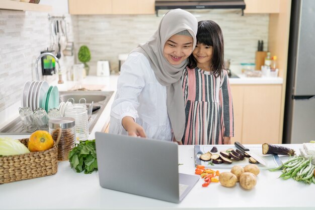 Glückliche muslimische asiatische Frau mit ihrer Tochter, die zusammen in der Küche kocht