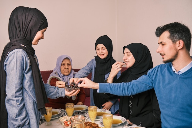 Glückliche muslimische Familie beim Iftar-Abendessen während des Ramadan-Esstischs, der Datteln isst, um schnell zu brechen