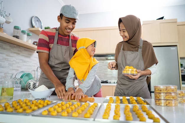 Glückliche muslimische Familie mit Hijab, die zu Hause zusammen Nastar-Kuchen macht. schöne eltern- und kinderkochaktivität für eid mubarak