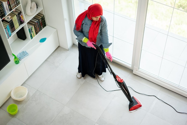 Glückliche muslimische Frau, die das Wohnzimmer des modernen Hauses putzt. Foto in hoher Qualität