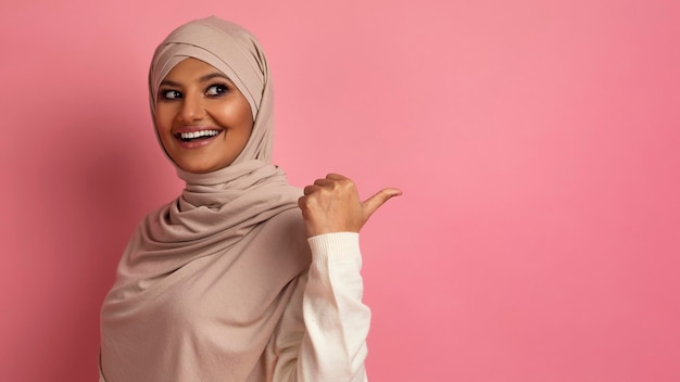 Glückliche muslimische Frau im Hijab, die auf den Kopierraum hinter ihrem Rücken zeigt
