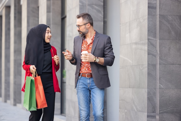 Glückliche muslimische Frau mit Einkaufstüten und Mann mit Kaffee zum Mitnehmen