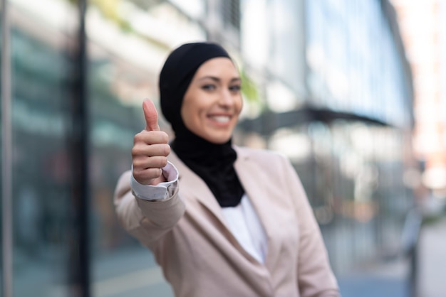 Glückliche muslimische Geschäftsfrau, die sich Daumen zeigt