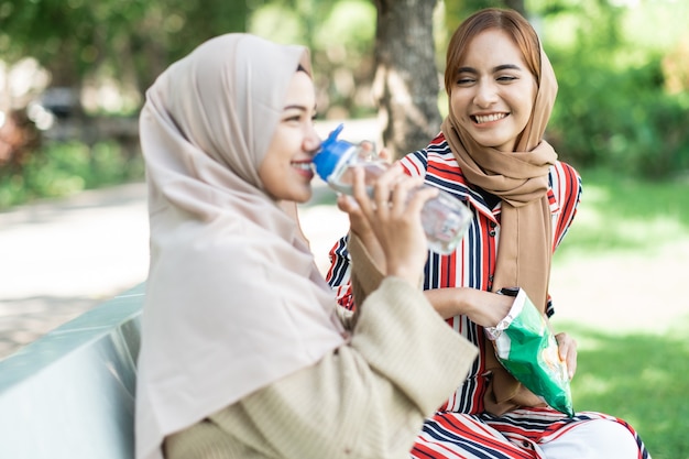 Glückliche muslimische junge Frau mit Freund genießen ihren Snack beim Entspannen im Park