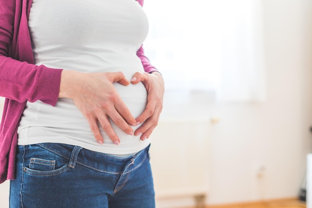 Glückliche Mutter bildet ein Herz auf ihrem schwangeren Bauch