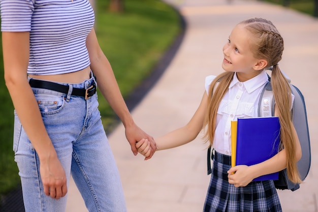 Glückliche Mutter bringt kleine Tochter Schulmädchen zur Schule