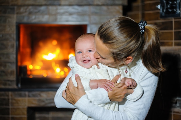 Glückliche Mutter, die Baby durch den Kamin küsst