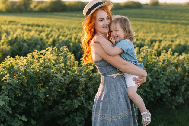 Glückliche Mutter, die ihre kleine Tochter auf einem grünen Feld hält