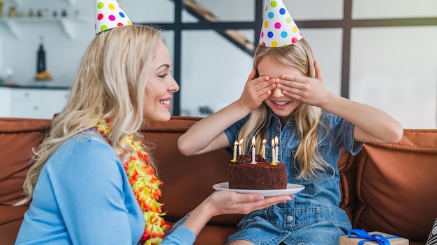 Glückliche Mutter, die ihre Tochter mit Geburtstagstorte überrascht