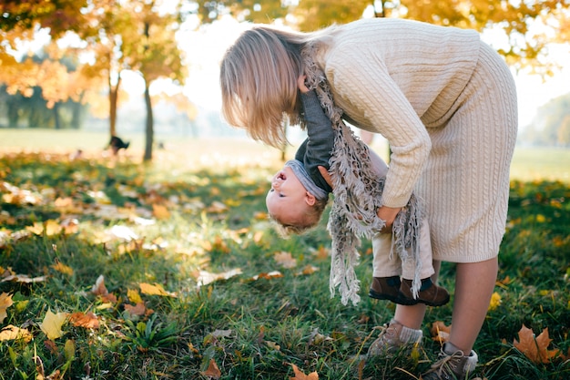 Glückliche Mutter, die Spaß mit ihrem Baby im Freien im Herbstpark hat.