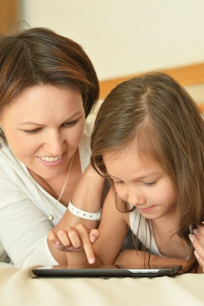 Glückliche Mutter, die Zeit mit kleiner Tochter im Bett mit Tisch-PC verbringt