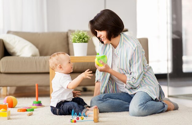 glückliche Mutter, die zu Hause einem kleinen Sohn einen Sippy Cup gibt