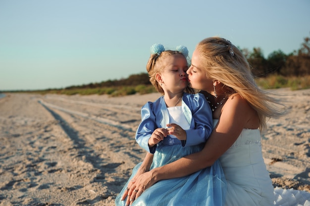 Glückliche Mutter im Hochzeitskleid mit ihrer Tochter am Strand.