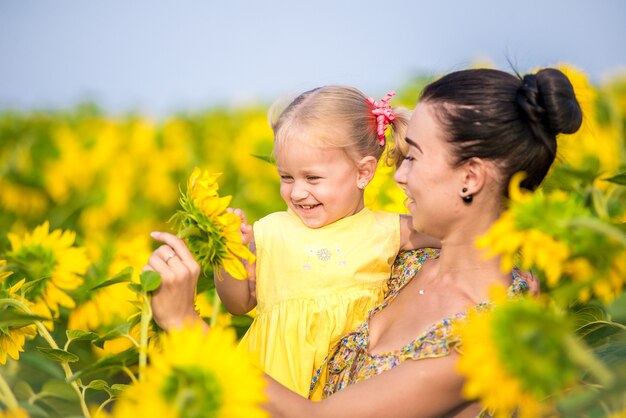 Glückliche Mutter mit der Tochter auf dem Feld mit Sonnenblumen