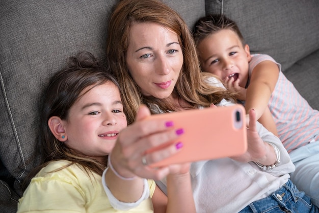 Glückliche Mutter mit ihren Kindern macht ein Selfie oder einen Videoanruf an Vater oder Verwandte auf einem Sofa Konzept der Technologie neue Generation Familienverbindung Elternschaft
