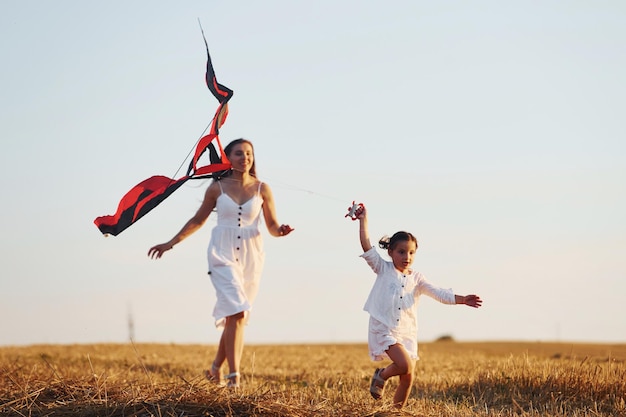 Glückliche Mutter mit ihrer kleinen Tochter hat Spaß beim Spielen mit Drachen im Freien auf dem Feld