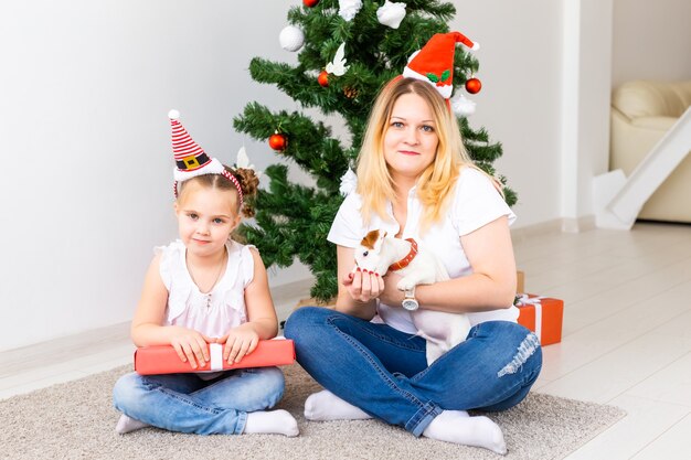 Glückliche Mutter mit ihrer Tochter und Jack Russell Terrier Hund sitzen in der Nähe des Weihnachtsbaumes