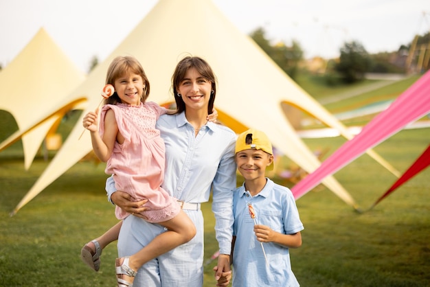 Glückliche Mutter mit kleinem Mädchen und Jungen besuchen einen Vergnügungspark