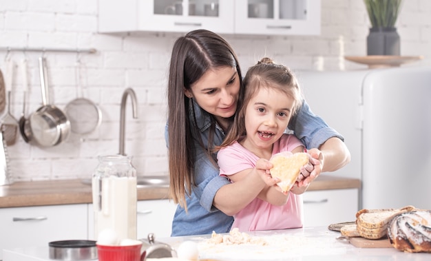 Glückliche Mutter mit Tochter, die hausgemachte Kuchen auf dem Hintergrund einer hellen Küche vorbereitet.