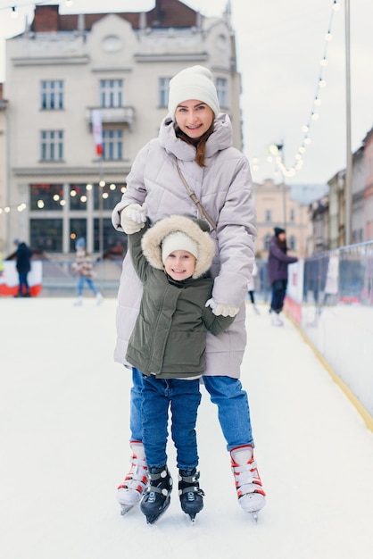 Glückliche Mutter mit Tochter, die im Winter Eislaufen auf einer städtischen Eisbahn unterrichtet