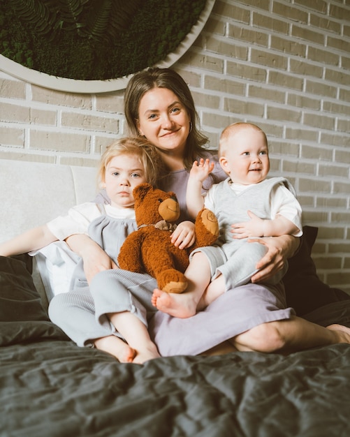 Glückliche Mutter mit zwei Kindern, die sich zu Hause auf einem großen Bett entspannen